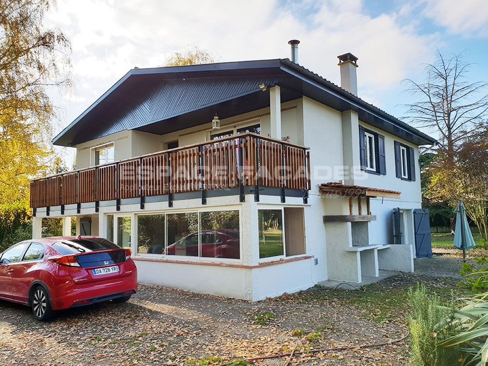 Maison moderne avec balcon en bois et une voiture rouge devant la façade