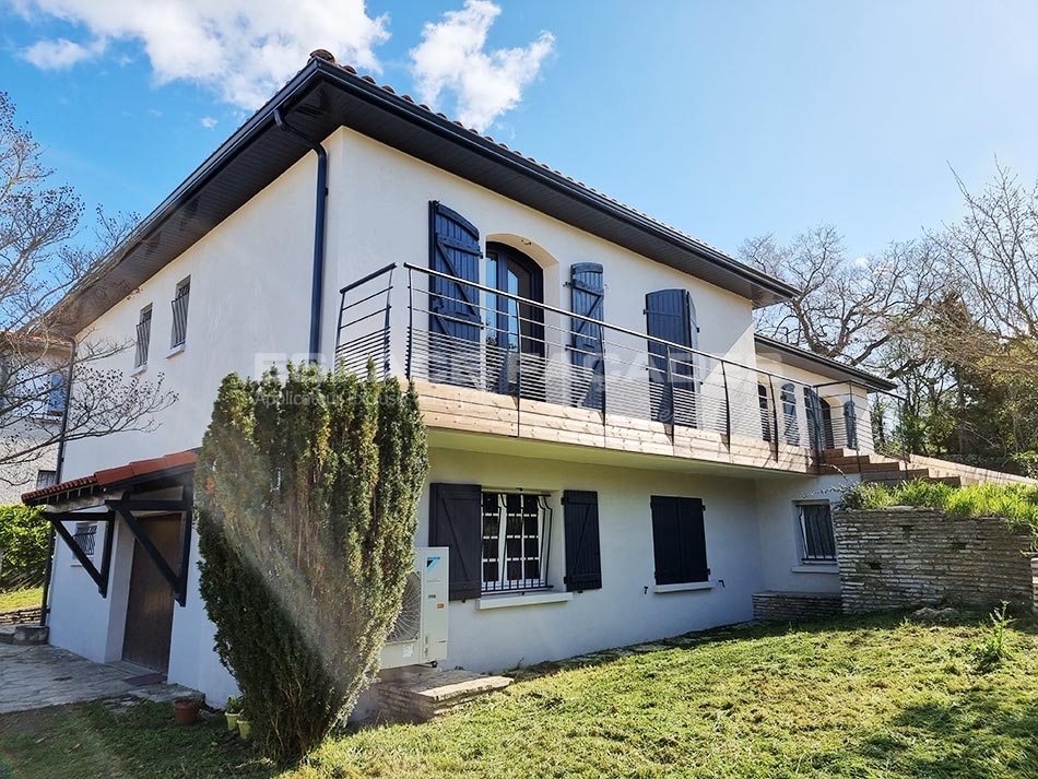 Maison avec façades blanches et balcons en bois, espaces extérieurs aménagés